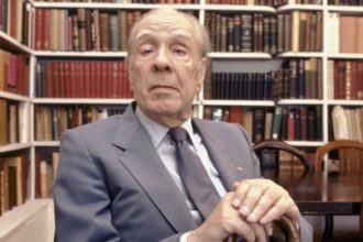 Foto do escritor Jorge Luis Borges, ao fundo estante de livro