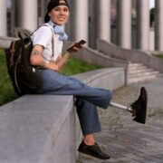 Foto de uma mulher jovem, sentada numa mureta, com uma prótese na perna. Meritocracia é um conceito discutível.