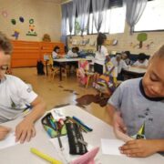 Foto de duas crianças na faixa dos 5 anos, numa sala de aula, desenhando. Essas são as mais prejudicadas por decretos antivacinas