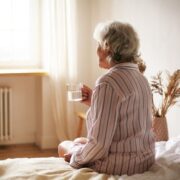 Senhora idosa, sentada na beira da cama segunda uma xícara, pessoas assim tem medo de chegar à velhice