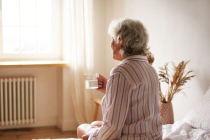 Senhora idosa, sentada na beira da cama segunda uma xícara, pessoas assim tem medo de chegar à velhice