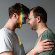 Na foto, no interior de algum lugar, dois jovens estão com a cabeça encontrada no outro, num deles reflete uma luz com po arco iris, Vida mais simples