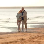 Foto de um casal de idosos abraçados, caminhando na areia da praia. Relacionamentos é um componente para conseguir viver 120 anos.