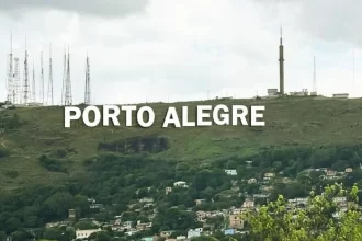 Foto simulando o letreiro como nome de Porto Alegre no alto de um morro da cidade. Ao fundo, antenas de transmissão.