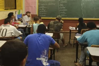 Foto de uma sala de aula do ensino médio. Alunos de costas, lousa o fundo. A influência da internet aumenta a violência nas escolas