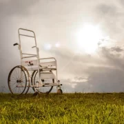 Foto de uma cadeira de rodas, símbolo de pessoas com deficiência. no meio de um gramado, sob um céu nublado.