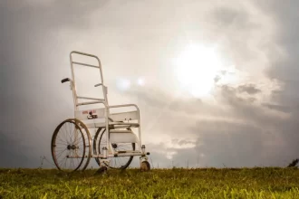 Foto de uma cadeira de rodas, símbolo de pessoas com deficiência. no meio de um gramado, sob um céu nublado.