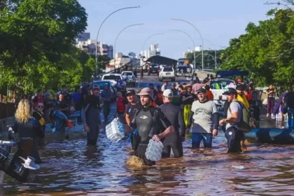 Foto da tragédia da enchente em Porto Alegre, voluntários no meio d'agua carregam mantimentos para as vítimas