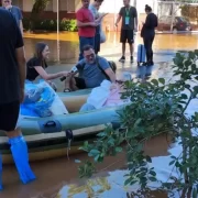 Foto de uma senhora sendo salva num bote (ou num berço) por voluntários, na enchente de porto alegre