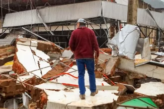Foto de um homem no meio de escombros da comunidade arrasada pela enchente do RS