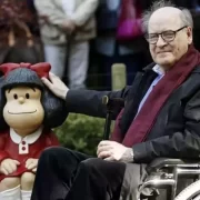 Foto do cartunista Quino, sentado numa cadeira de rodas com a sua principal criação, a Mafalda, em formato de boneca ao seu lado.