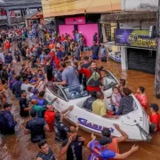 Foto de dezenas de pessoas numa rua inundada pela água na cidade de Canoas, no RS. Cada pessoa ajuda como pode.