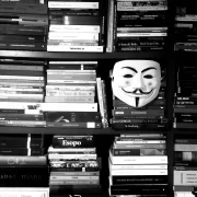 Foto de estante de livros de literatura em preto e branco, com uma máscara pendurada