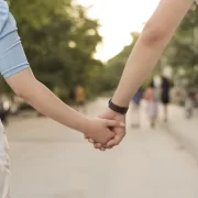 Foto de um casal de mãos dadas, na imagem só aparece meio corpo de cada um e se vê que estão num parque. Amor