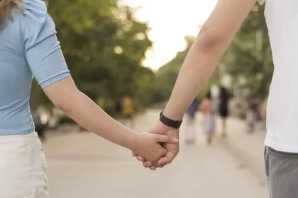 Foto de um casal de mãos dadas, na imagem só aparece meio corpo de cada um e se vê que estão num parque. Amor