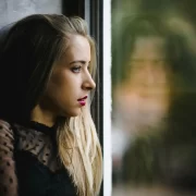Mulher jovem olhando pela janela, reflexo no vidro. Anorexia de afetos.