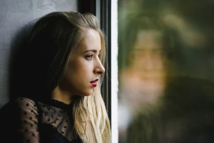 Mulher jovem olhando pela janela, reflexo no vidro. Anorexia de afetos.