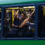 Foto da janela de um ônibus cheio em deslocamento, com pessoas apertadas. Corpo espremido.