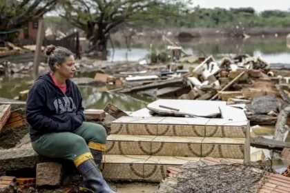 Foto de uma mulher sentada ao lado da sua casa destruída pela enchente. candidata à migração