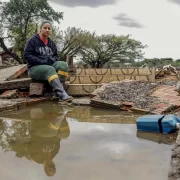 Foto de uma mulher numa casa derrubada pela enchente no RS. Cidades inteiras foram varridas.