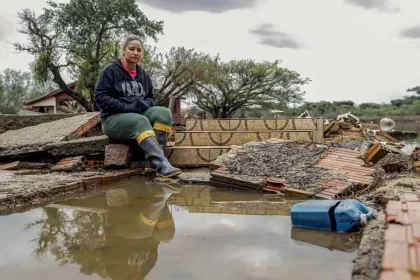 Foto de uma mulher numa casa derrubada pela enchente no RS. Cidades inteiras foram varridas. A recuperação vai demorar