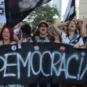 Foto de uma manifestação a favor da democracia, mulher carregam uma grande faixa.