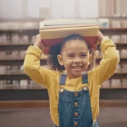 Foto de uma menina carregando livros na cabeça. Livros são fundamentais na educação