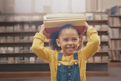 Foto de uma menina carregando livros na cabeça. Livros são fundamentais na educação