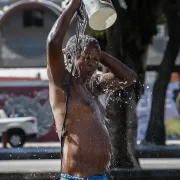 Foto de um homem, sem camisa derrubando na cabeça um balde de água. Ondas de frio e calor vão se intercalar.