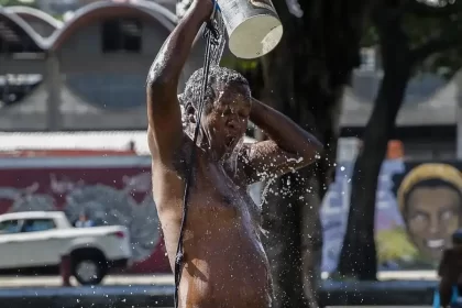 Foto de um homem, sem camisa derrubando na cabeça um balde de água. Ondas de frio e calor vão se intercalar.