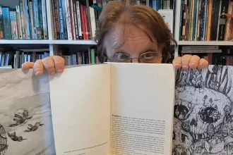 Foto da jornalista Lelei Teixeira olhando por trás do seu livro