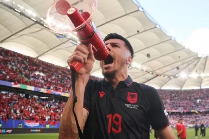 Foto do atacante albanês Mirlind Daku com um megafone em punho protestando contra os sérvios