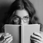 Mulher de óculos tem um livro aberto em frente ao rosto.
