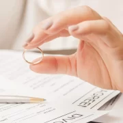 Foto de uma mão feminina segurando uma aliança sobre um contrato, o pacto antenupcial é uma alternativa para os casais