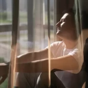 Foto de um homem sentado na janela pegando sol. O sol é um dos meios de adquirir vitamina D