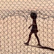 Foto de uma menina caminhando num campo de futebol de areia, aspectos das cidades