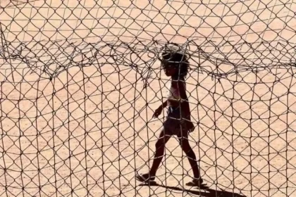 Foto de uma menina caminhando num campo de futebol de areia, aspectos das cidades