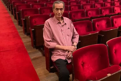 Foto do compositor Verocai, sentado numa cadeira de uma plateia de um teatro