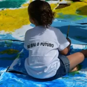 Foto de uma criança pequena sentada no chão de uma classe escolar. Elas são o objetivo da cidade educadora