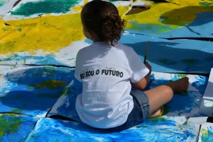 Foto de uma criança pequena sentada no chão de uma classe escolar. Elas são o objetivo da cidade educadora