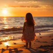 Foto de uma menina pequena na beira da praia e dirige o olhar para o mar num fim de tarde