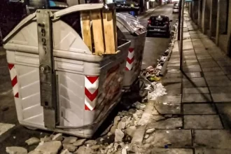 Foto de um Contêiner numa rua de porto alegre, com as sacolas de lixo espalhadas pelo chão