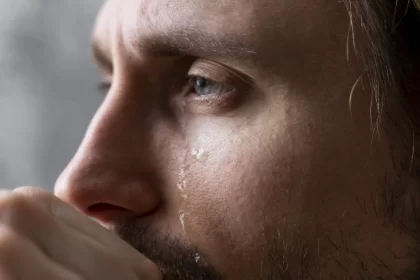 Foto fechada no rosto de um homem branco, jovem adulto, dos olhos escorrem lágrimas