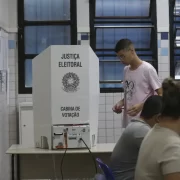 Foto de uma urna com um eleitor jovem votanto