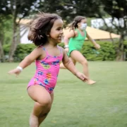 Imagem de uma menina com nanismo, de maiô, correndo por um gramado. Autora fala de diferença e inclusão