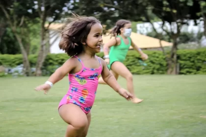 Imagem de uma menina com nanismo, de maiô, correndo por um gramado. Autora fala de diferença e inclusão