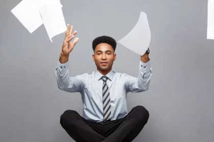 Homem negro, sentado no chão, vestido com roupas sociais, de gravata, joga papeis para o alto. Chega de escala 6x1