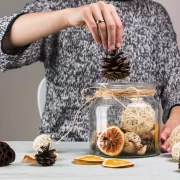 Mulher colocando pinhas secas num pote, para fazer um pot-pourri