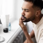 Homem negro, jovem, examina a pele negra no espelho