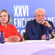 Foto de Lula e Gleisi Hoffmann sentados numa bancada de um evento